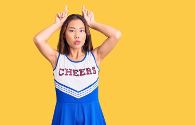 Genç, güzel Çinli kız amigo kız üniforması giyiyor ve parmağıyla boynuz gibi komik hareketler yapıyor. 