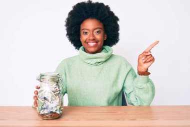 Genç Afrikalı Amerikalı kadın elinde kavanozla gülümsüyor mutlu bir şekilde elini ve parmağını yana uzatıyordu. 