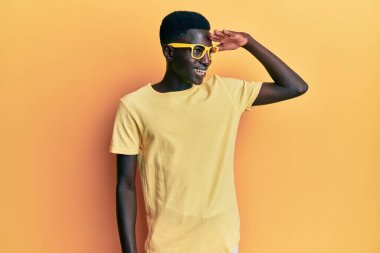 Gündelik kıyafetler ve gözlük takan genç Afro-Amerikan bir adam çok mutlu ve tebessüm ediyor. arama kavramı. 