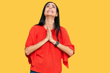 Güzel, genç bir kadın gündelik giysiler giyip elleri bağlı yalvarıyor ve dua ediyor. Yüzünde umut ifadesi var. Çok duygusal ve endişeli. Yalvarıyor. 