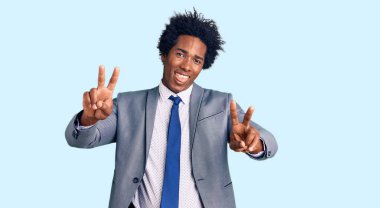 Afro saçlı, iş ceketi giyen, ağzı açık gülümseyen, iki elini de zafer işareti yapan yakışıklı Afro-Amerikalı adam. İki numara.. 