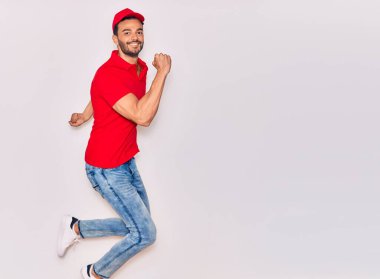 Mutlu gülümseyen üniformalı yakışıklı İspanyol teslimatçı. Yüzünde tebessümle zıplıyor, beyaz arka planda yumruklar havada kutluyor..