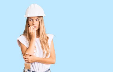 Sarışın, sapkalı, boyalı elbiseli, stresli ve gergin görünen elleri ağızdan tırnak yiyen güzel beyaz bir kadın. anksiyete. 