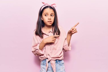 Gündelik kıyafetler giyen güzel bir kız çocuğu iki eliyle endişeli ve endişeli bir ifadeye işaret ediyor. 