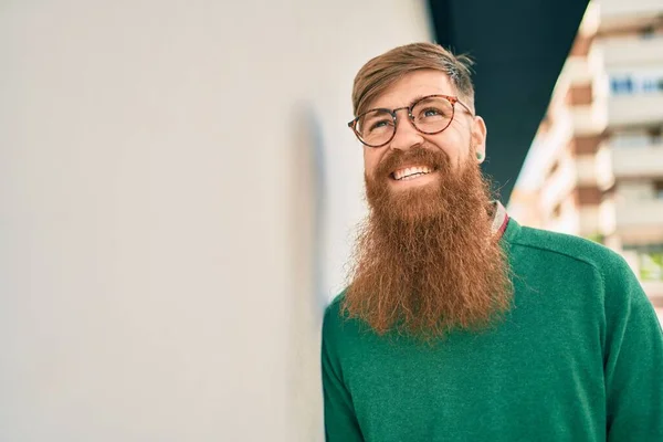 市内の壁にもたれて幸せな笑顔で赤毛のひげを持つ若いアイルランドの男 — ストック写真