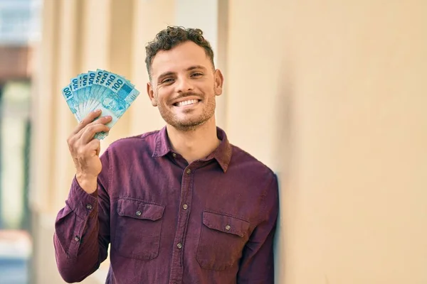 Joven Hispano Sonriendo Feliz Sosteniendo Billetes Reales Brasileños Ciudad —  Fotos de Stock