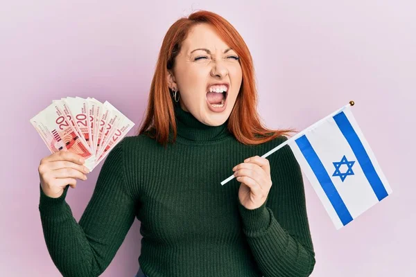 漂亮的红头发女人手里拿着20先令钞票和以色列国旗 怒气冲冲地尖叫着 怒气冲冲地大叫着 愤怒和好斗的概念 — 图库照片