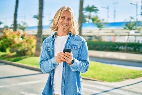 Young blond scandinavian man smiling happy using smartphone at the city.