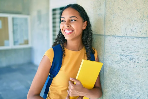 Genç Afrikalı Amerikalı öğrenci mutlu gülümsüyor ve üniversitede kitap tutuyor..