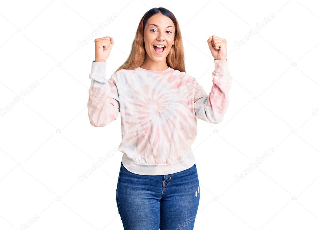 Beautiful young woman wearing casual tie dye sweatshirt screaming proud, celebrating victory and success very excited with raised arms 