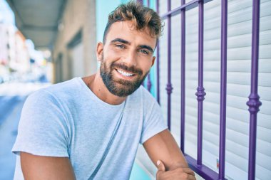 Genç İspanyol adam gülümsüyor. Mutlu bir şekilde şehrin duvarına yaslanıyor.