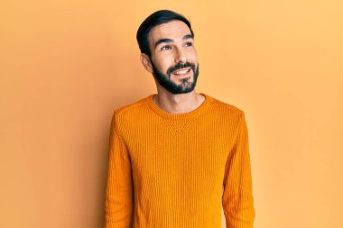 Gündelik kıyafetler giyen genç İspanyol bir adam yüzünde gülümsemeyle yan yana bakıyor, doğal bir ifade. Kendinden emin gülen. 