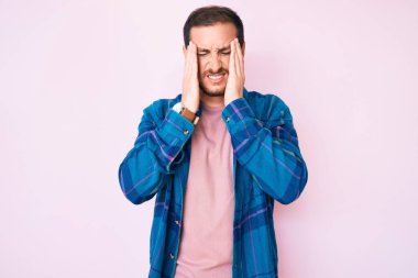 Elleri başının üstünde, günlük kıyafetler giyen genç yakışıklı bir adam. Stres yüzünden başı ağrıyor. migren ağrısı. 