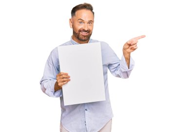 Boş pankart tutan yakışıklı orta yaşlı adam gülümsüyor. Elleri ve parmakları yana doğru uzanıyor. 