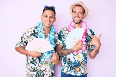 Yazlık tişört giyen iki genç gay el ele tutuşup gülümsüyor. 