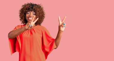 Gündelik giysiler giymiş genç Afro-Amerikan kadın kameraya bakıp zafer işareti yapıyor. İki numara.. 