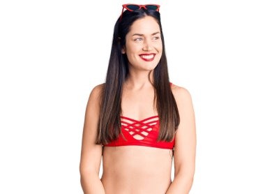 Genç, beyaz, güzel bir kadın bikini giyiyor. Yüzünde gülümseme, doğal bir ifade var. Kendinden emin gülen. 