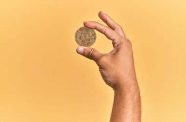 Genç İspanyol el, bitcoin 'i izole edilmiş sarı arka planda tutuyor..