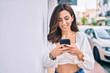 Genç İspanyol kadın şehirde akıllı telefon kullanarak mutlu bir şekilde gülümsüyor..