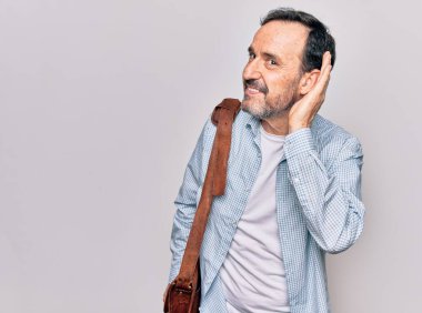 Orta yaşlı yakışıklı iş adamı, izole edilmiş beyaz arka planda deri çanta takıyor, sırıtarak dedikodu ve dedikoduları dinliyor. Sağırlık kavramı.