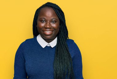 Saçları örgülü, mutlu ve havalı bir gülümsemesi olan genç siyahi bir kadın. şanslı kişi. 