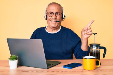 Ofiste çalışan gri saçlı, kıdemli yakışıklı adam operatör kulaklığı takıyor, gülümsüyor. 