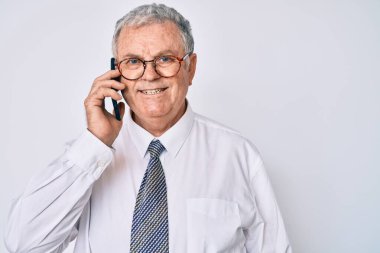 Kıdemli gri saçlı adam iş kıyafetleri giymiş akıllı telefondan konuşuyor. Pozitif ve mutlu görünüyor. Kendine güvenen bir gülümsemeyle dişlerini gösteriyor. 