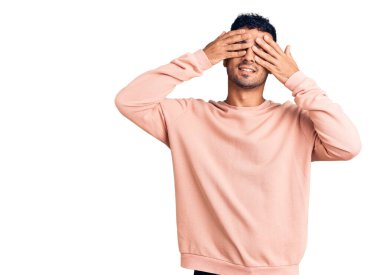 Latin asıllı genç adam günlük kıyafetler giyiyor. Gözleri kapatıyordu. Neşeli ve komik gülümsüyordu. kör kavram. 