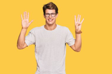 Yakışıklı beyaz adam, günlük kıyafetler ve gözlük takıyor. Dokuz numarayı gösteriyor ve işaret ediyor. Kendinden emin ve mutlu bir şekilde gülümsüyor.. 