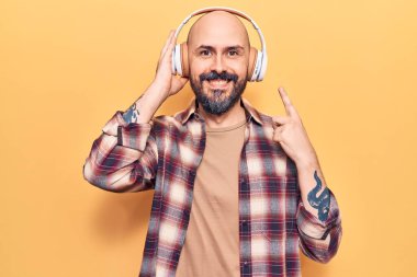 Genç yakışıklı adam kulaklık takarak müzik dinliyor mutlu bir şekilde el ve parmak işareti yapıyor. 