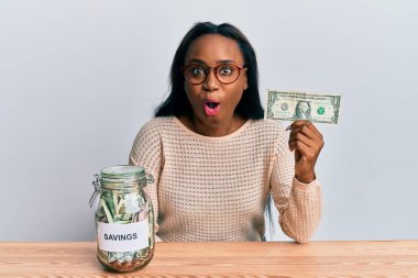 Genç Afrikalı bir kadın elinde dolar ve kavanozla birikimlerini elinde tutuyor. Şaşırmış ve şaşırmış bir şekilde ağzı açık kalmış, inançsız bir yüz. 
