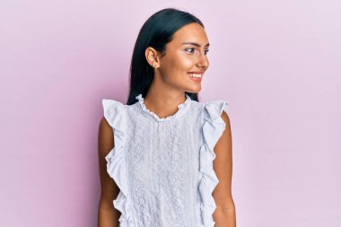 Zarif bir yaz tişörtü giyen genç esmer kadın, yan bakmak için, rahat profil pozu doğal bir yüz ve kendinden emin bir gülümseme ile. 