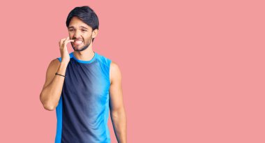 Spor kıyafetleri giyen yakışıklı İspanyol adam gergin ve gergin görünüyor. Ağzı tırnak yiyen ellerle. anksiyete. 