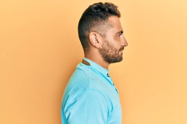 Sakallı, sıradan kıyafetler giyen, rahat bir görünüm takınan, kendine güveni olan yakışıklı bir adam.. 