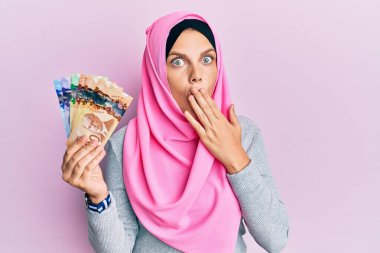 İslami tesettüre bürünmüş genç beyaz kadın elinde Kanada doları banknotları tutuyordu. Ağzı elle kaplayan banknotlar, şok olmuş ve hata yapmaktan korkan. şaşırmış ifade 