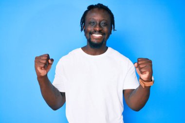 Örgülü beyaz tişörtlü genç Afro-Amerikalı adam gururla bağırıyor zaferi ve başarıyı kollarını kaldırarak kutluyor. 