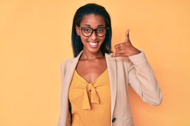 Genç Afro-Amerikan kadın iş kıyafetleri içinde gülümsüyor telefonla el ve parmak hareketleri yapıyor telefonda konuşuyor gibi. iletişim kavramları. 