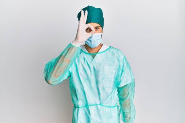 Cerrah üniforması ve tıbbi maske takan genç yakışıklı adam el hareketleriyle gülümsüyor ve mutlu yüzüyle parmaklarının arasından bakıyor.. 