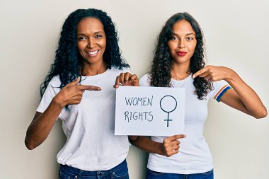 Afrika kökenli Amerikalı anne ve kız ellerinde kadın hakları afişi mutlu bir şekilde parmakla gösteriyorlar. 