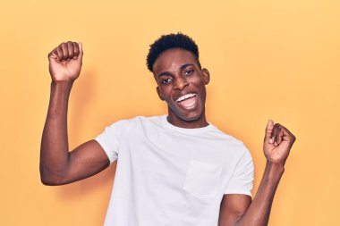 Genç Afro-Amerikan erkeği gündelik kıyafetler giymiş mutlu ve neşeli dans ediyor, gülümsüyor rahat ve kendinden emin bir şekilde müzik dinliyor. 