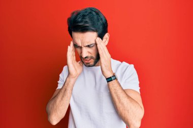 Latin asıllı genç bir adam, günlük beyaz tişört giyiyor, eli başının üstünde, stresten baş ağrısı çekiyor. migren ağrısı. 