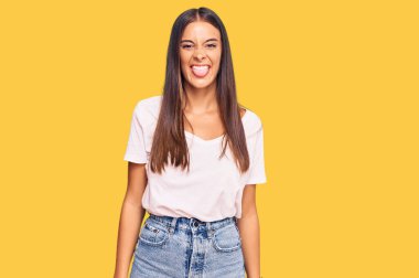 Günlük beyaz tişört giyen genç İspanyol kadın komik bir ifadeyle dilini dışarı çıkarıyor. duygu kavramı. 