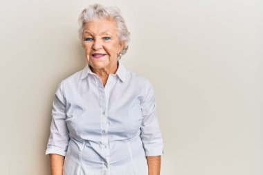 Yaşlı, gri saçlı, sıradan kıyafetler giyen, yüzünde mutlu ve havalı bir gülümseme olan bir kadın. şanslı kişi. 