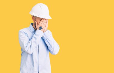 Mimar şapkası takan genç yakışıklı bir adam. Ağlarken suratını ellerle kapatıyor. depresyon kavramı. 