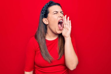 Genç, güzel, esmer bir kadın, günlük tişört giyip izole edilmiş kırmızı arka planda durmuş el ele tutuşarak bağırıyor ve bağırıyordu. İletişim konsepti.