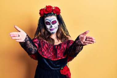 Sarı üzerine ölü kostümü giymiş genç bir kadın kameraya bakıp sarılmak için kollarını açmış gülümsüyor. Mutluluğu kucaklayan neşeli bir ifade.. 