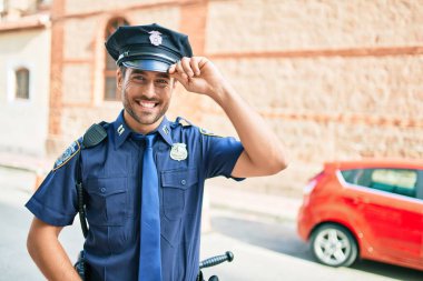 Polis üniforması giyen genç, yakışıklı İspanyol polis mutlu bir şekilde gülümsüyor..