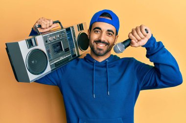 Kasetçalar tutan genç İspanyol adam mikrofonla şarkı söylerken yüzünde mutlu ve havalı bir gülümsemeyle gülümsüyor. diş gösterme. 