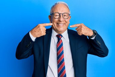 İş elbisesi giyen, kravatlı, neşeli gülümseyen, parmaklarıyla ve ağzıyla işaret eden kıdemli beyaz adam. diş sağlığı kavramı. 