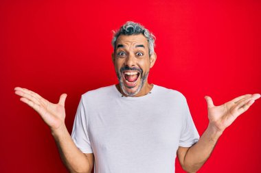 Orta yaşlı beyaz tişört giyen, mutlu bir gülümsemeyle zaferi kutlayan gri saçlı bir adam ve ellerini kaldırarak kazanan bir ifade. 